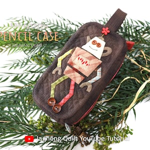 May include: PDF pattern for a robot-shaped pencil case. The case is brown with a red zipper and a robot applique. The robot has a white face with brown eyes and a red flower on its head.
