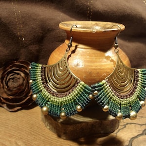 Peut inclure: Une paire de boucles d'oreilles en macramé vert et marron avec des accents en métal doré. Les boucles d'oreilles sont suspendues à une surface en bois.