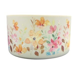 May include: A white ceramic container with a floral pattern. The pattern features pink, orange, and yellow flowers with green leaves.