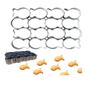 May include: A set of 16 silver metal fish-shaped cookie cutters, arranged in a rectangular grid. A smaller set of 18 silver metal cookie cutters in a rectangular shape is also included. There are 8 fish-shaped cookies scattered on a white background.