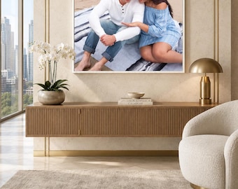May include: A rectangular custom photo canvas print featuring a couple sitting on a beach, displayed in a white frame on a wall above a wooden console table. The text CUSTOM PHOTO CANVAS is printed below the image with the tagline Your memories, beautifully displayed.