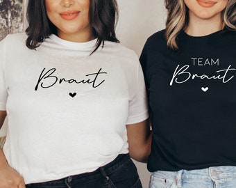 Puede incluir: Dos camisetas blancas con texto negro. Una camiseta dice "Braut" con un pequeño corazón. La otra camiseta dice "Team Braut" con un pequeño corazón.