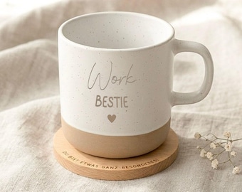 May include: A white ceramic mug with a speckled finish and a tan base, featuring the text "Work BESTIE" and a small heart icon. The mug sits on a round wooden coaster with the engraved German text "DU BIST ETWAS GANZ BESONDERES".