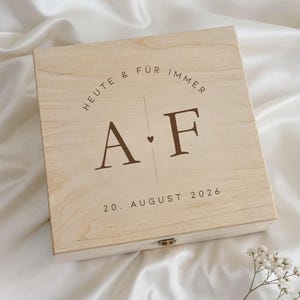Könnte beinhalten: Eine hellfarbene Holzkiste mit Scharnierdeckel. Die Kiste ist mit dem Text "HEUTE & FÜR IMMER" und den Initialen "A" und "F" graviert, die durch eine vertikale Linie und ein Herz getrennt sind. Das Datum "20. AUGUST 2026" ist ebenfalls aufgedruckt.