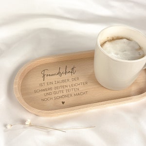 May include: A wooden tray with the text "Freundschaft ist ein Zauber, der schwere Zeiten leichter und gute Zeiten noch sch&ouml;ner macht" engraved on it. A white ceramic mug with coffee is sitting on the tray.