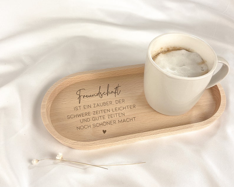 May include: A wooden tray with the text "Freundschaft ist ein Zauber, der schwere Zeiten leichter und gute Zeiten noch sch&ouml;ner macht" engraved on it. A white ceramic mug with coffee is sitting on the tray.