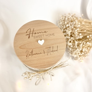 Op de afbeelding: Een houten deksel voor een kaarsenpot met de tekst "Home Sweet Home" en een klein wit hart. Het deksel is gepersonaliseerd met de namen "Katharina & Michael".