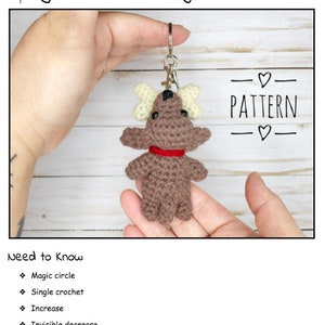 May include: A crocheted dog keychain with bone-shaped accents and a red collar. The keychain is held in front of a light-colored wooden background. The text "Dog with a Bone Keychain Pattern" and "PATTERN" are visible.