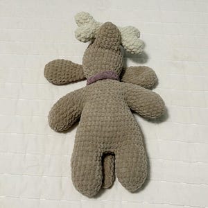 May include: A brown crocheted reindeer plush toy with white antlers and a purple ribbon around its neck.