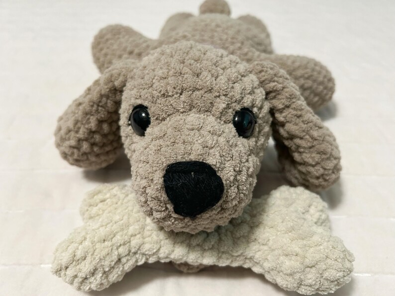 May include: A plush grey and white dog toy with a bone in its mouth. The dog has black eyes and a black nose.