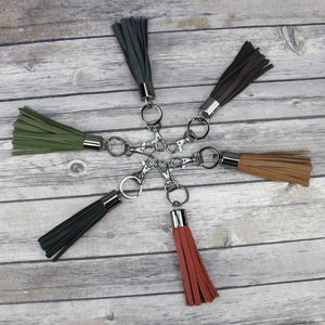 May include: Six keychains with different colored tassels and silver key rings. The tassels are black, green, brown, tan, and red.