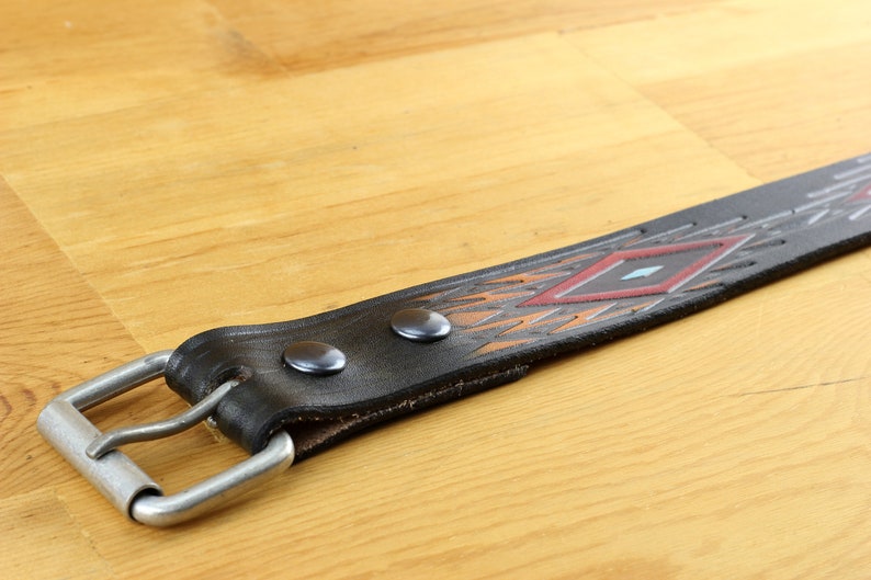 May include: A black leather belt with a geometric pattern in shades of orange, red, and blue. The belt has a silver buckle and two silver rivets.