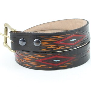 May include: A brown leather belt with a geometric pattern in orange, red, and blue. The belt has a brass buckle and two metal rivets.