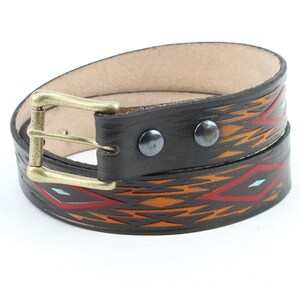 May include: A brown leather belt with a geometric pattern in orange, red, and blue. The belt has a brass buckle and is decorated with silver rivets.