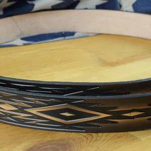 May include: Close-up of a black leather belt with a geometric pattern embossed in a light brown colour. The belt is folded in half and the pattern is visible on both sides.