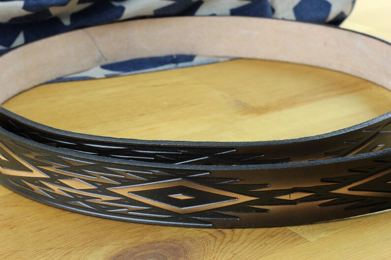 May include: Close-up of a black leather belt with a geometric pattern embossed in a light brown colour. The belt is folded in half and the pattern is visible on both sides.