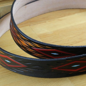 May include: Two black leather belts with a geometric pattern of red, orange and white diamonds. The belts are stacked on top of each other.