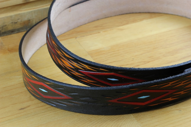 May include: Two black leather belts with a geometric pattern of red, orange and white diamonds. The belts are stacked on top of each other.
