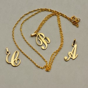 May include: Three gold necklaces with initial pendants. The pendants are in a cursive font and spell out the letters A, B, and C.