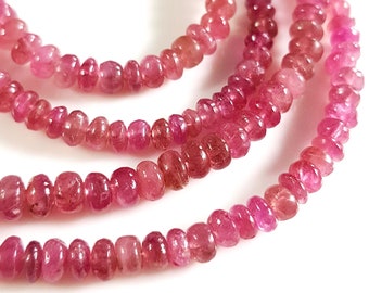 May include: A strand of pink tourmaline beads. The beads are small and round, and they are strung on a clear thread. The beads are arranged in a loose, flowing pattern.