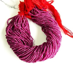 Op de afbeelding: Een streng dieproze robijn kralen, ongeveer 2 mm in diameter, met een rode kwast aan het einde.