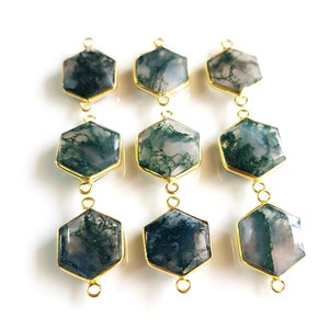 May include: Nine hexagonal moss agate gemstone pendants with gold-colored metal edging. The gemstones display a mix of green, white, and gray patterns. Each pendant has a loop at the top and bottom for attaching to a chain or other jewelry component.