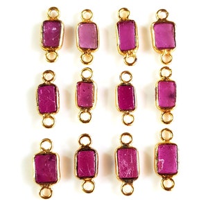 Peut inclure: Douze breloques connecteurs dorés avec une pierre précieuse rectangulaire rose au centre. Chaque breloque a deux boucles de chaque côté pour l'attacher à des bijoux.
