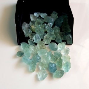 May include: A pile of light blue and green aquamarine rough gemstones. The gemstones are various sizes and shapes.