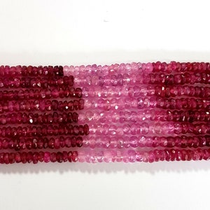 May include: A strand of pink and red gemstone beads. The beads are faceted and have a slightly irregular shape. The beads are strung on a clear thread.