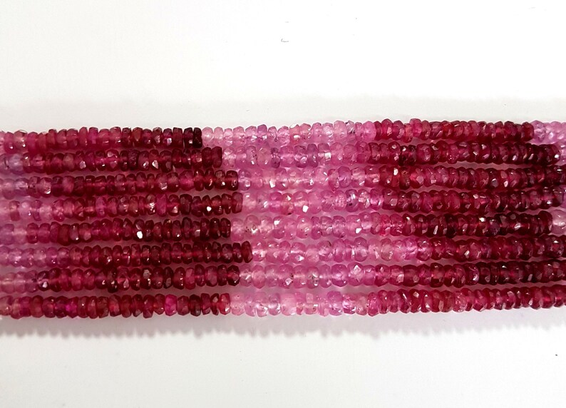 May include: A strand of pink and red gemstone beads. The beads are faceted and have a slightly irregular shape. The beads are strung on a clear thread.