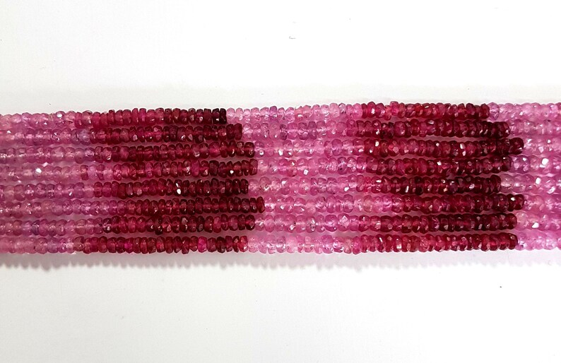 May include: A strand of pink and red gemstone beads. The beads are faceted and have a slightly irregular shape. The beads are strung on a clear thread.