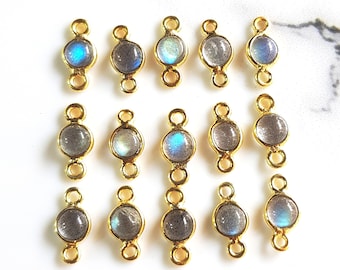 May include: A collection of fourteen gold-toned metal jewelry connectors, each featuring a circular labradorite gemstone. The stones display iridescent blue and grey flashes within a smooth bezel setting, with small loops at the top and bottom.