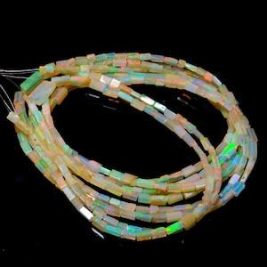 Może przedstawiać: Szereg białych koralików z opalu z iryzującymi zielonymi i pomarańczowymi błyskami. Koraliki są prostokątne i mają polerowane wykończenie.