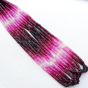 May include: A strand of faceted ruby beads in a gradient of pink, red, and purple shades. The beads are small and round, and they are strung on a clear thread.