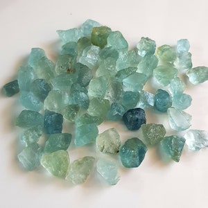 May include: A collection of rough aquamarine gemstones in various shades of blue and green. The stones are irregular in shape and have a natural, unpolished finish.
