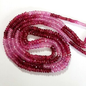 May include: A strand of pink and red gemstone beads. The beads are faceted and have a slightly irregular shape. The strand is approximately 18 inches long.