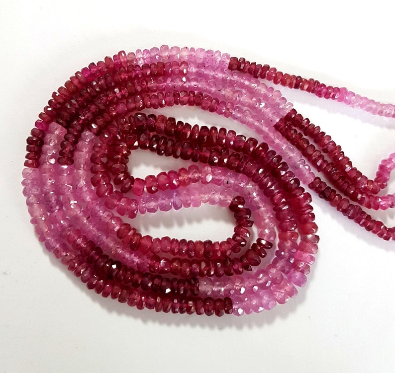 May include: A strand of pink and red gemstone beads. The beads are faceted and have a slightly irregular shape. The strand is approximately 18 inches long.