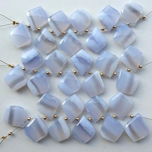 Può includere: Una collezione di perline di pietre preziose a forma di diamante blu chiaro. Ogni perla è sfaccettata e infilata con perline color oro e filo sottile. Le perle hanno una qualità traslucida con venature bianche e grigie.