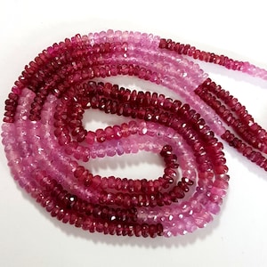 May include: A strand of pink and red gemstone beads. The beads are faceted and have a slightly irregular shape. The strand is approximately 18 inches long.