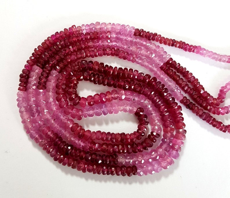 May include: A strand of pink and red gemstone beads. The beads are faceted and have a slightly irregular shape. The strand is approximately 18 inches long.