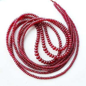 May include: A strand of deep red ruby beads, strung together in a circular shape. The beads are smooth and polished, with a slight variation in size.