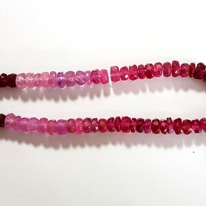 May include: A strand of pink and red gemstone beads. The beads are faceted and have a slightly irregular shape. The beads are strung on a clear thread.