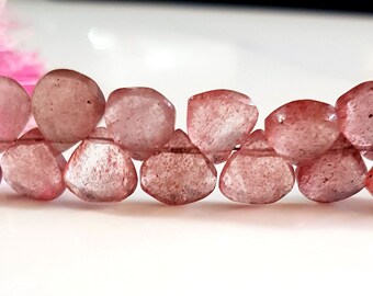 May include: A strand of faceted, heart-shaped strawberry quartz beads in shades of translucent pink and red with natural internal inclusions. The beads are arranged in a horizontal line, showcasing their polished surfaces and irregular, organic shapes.