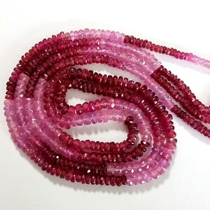 May include: A strand of pink and red gemstone beads. The beads are faceted and have a slightly irregular shape. The beads are strung on a clear thread.