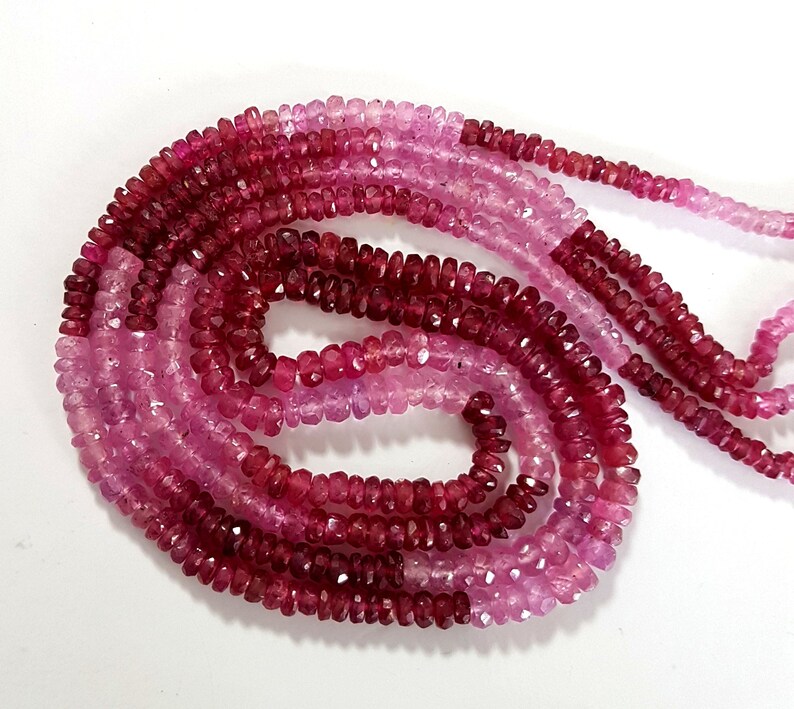 May include: A strand of pink and red gemstone beads. The beads are faceted and have a slightly irregular shape. The beads are strung on a clear thread.