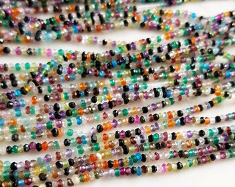 May include: A strand of colorful gemstone beads, including black, green, red, orange, purple, and blue beads. The beads are faceted and have a variety of shapes and sizes.