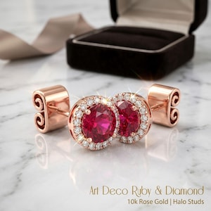 Könnte beinhalten: Ein Paar Ohrstecker aus 10-karätigem Roségold mit runden roten Rubinen, die von kleinen weißen Diamanten umgeben sind. Die Ohrringe verfügen über einen sicheren Steckverschluss und werden mit dem Text Art Deco Ruby & Diamond 10k Rose Gold Halo Studs präsentiert.
