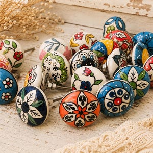 May include: A collection of colorful ceramic cabinet knobs with floral designs. The knobs feature various colors, including blue, orange, white, and green, with intricate hand-painted patterns. Each knob has a metal screw for easy installation.