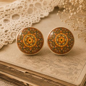 May include: Two decorative cabinet knobs with a cream base and a detailed orange, yellow, and brown mandala design. The knobs are round and have a glossy finish. They are placed on a vintage book.