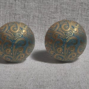 May include: Two decorative spheres with a teal base and gold swirling patterns. The spheres are round and appear to be made of a solid material. The gold pattern is detailed and covers most of the surface.
